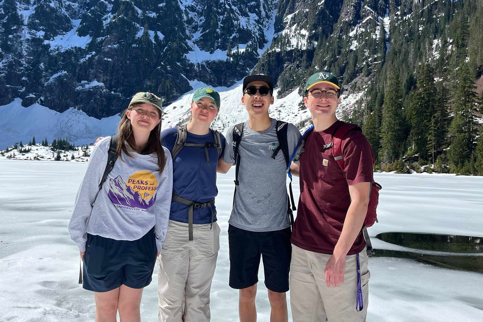 four students smiling and standing in front of glacial lake